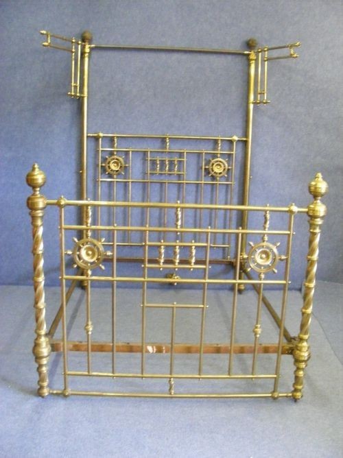 A Victorian polished brass half tester bedstead featuring intricate vertical spindles, rosette medallions, and barley twist corner posts.