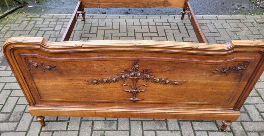 A late nineteenth-century French carved walnut bedstead with a panelled headboard, low footboard, and carved floral garlands. View III