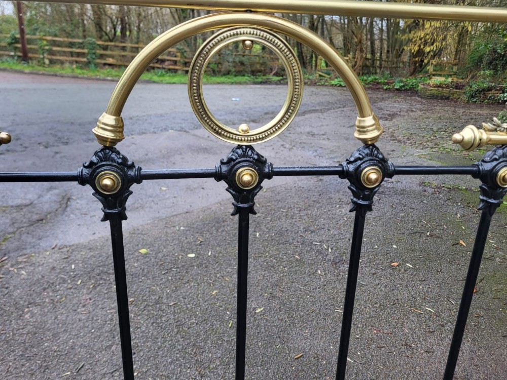 A Victorian double bedstead constructed from black-painted iron vertical spindles with top brass rails, brass finials, and central ornamental brass motifs. View IV