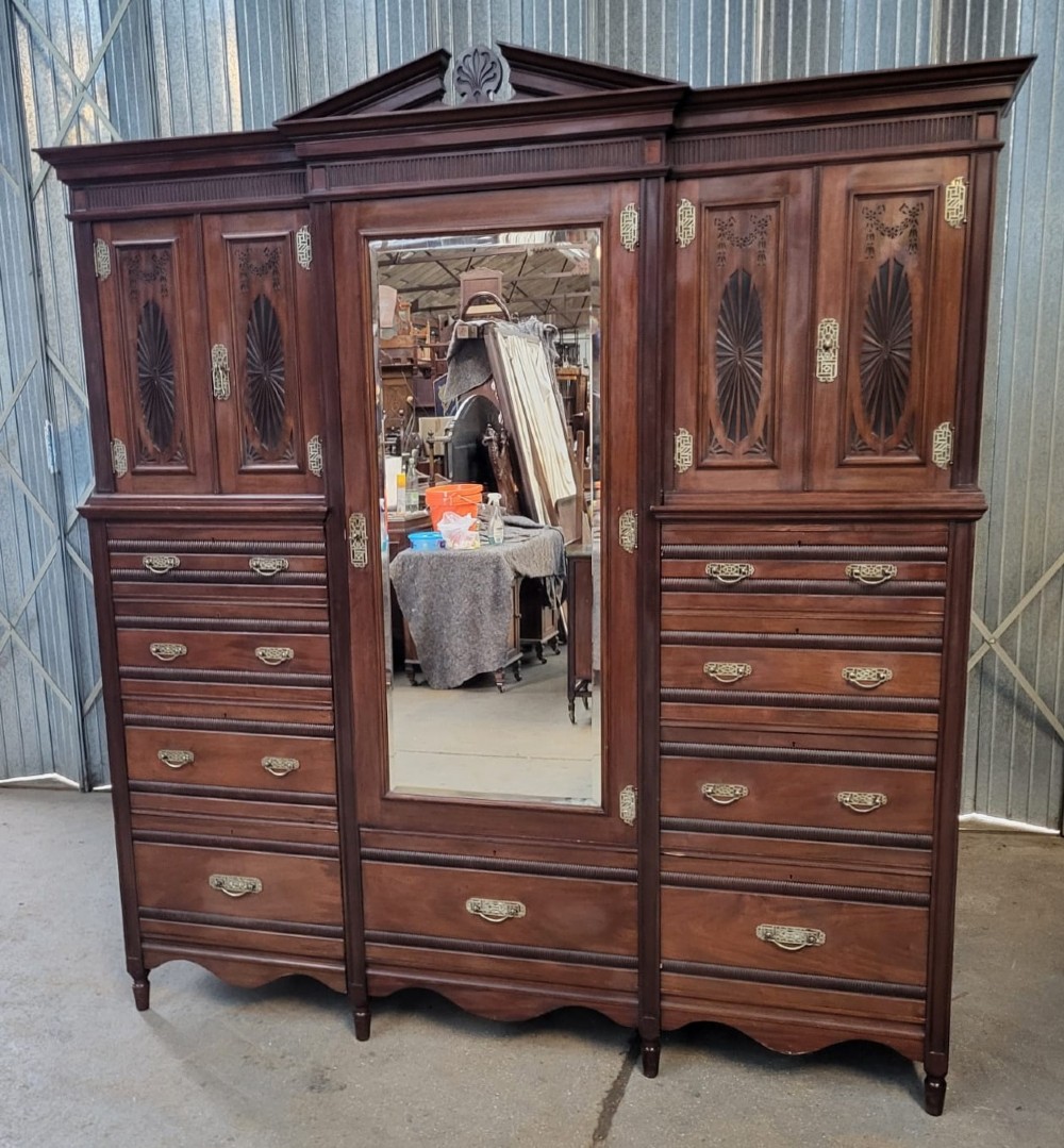 An Edwardian walnut bedroom suite comprising a breakfront compactum wardrobe with a central mirrored door alongside a matching dressing table with drawers and a swivel mirror. View III