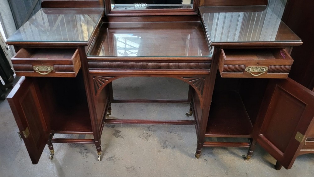 An Edwardian walnut bedroom suite comprising a breakfront compactum wardrobe with a central mirrored door alongside a matching dressing table with drawers and a swivel mirror. View VIII