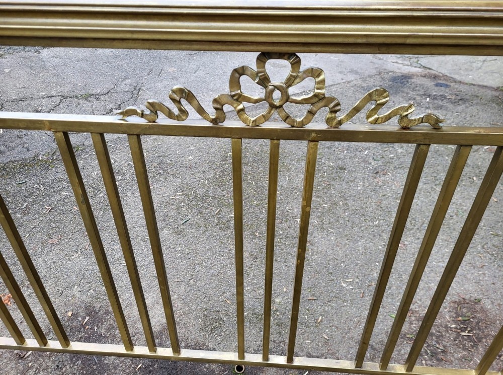 A Victorian king size brass bedstead featuring vertical spindles, an ornamental ribbon swag motif, and brass tubular frames on castors. View IV