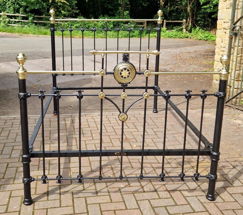 A Victorian king size black cast iron and polished brass bedstead featuring decorative central brass medallion detailing and top rails.