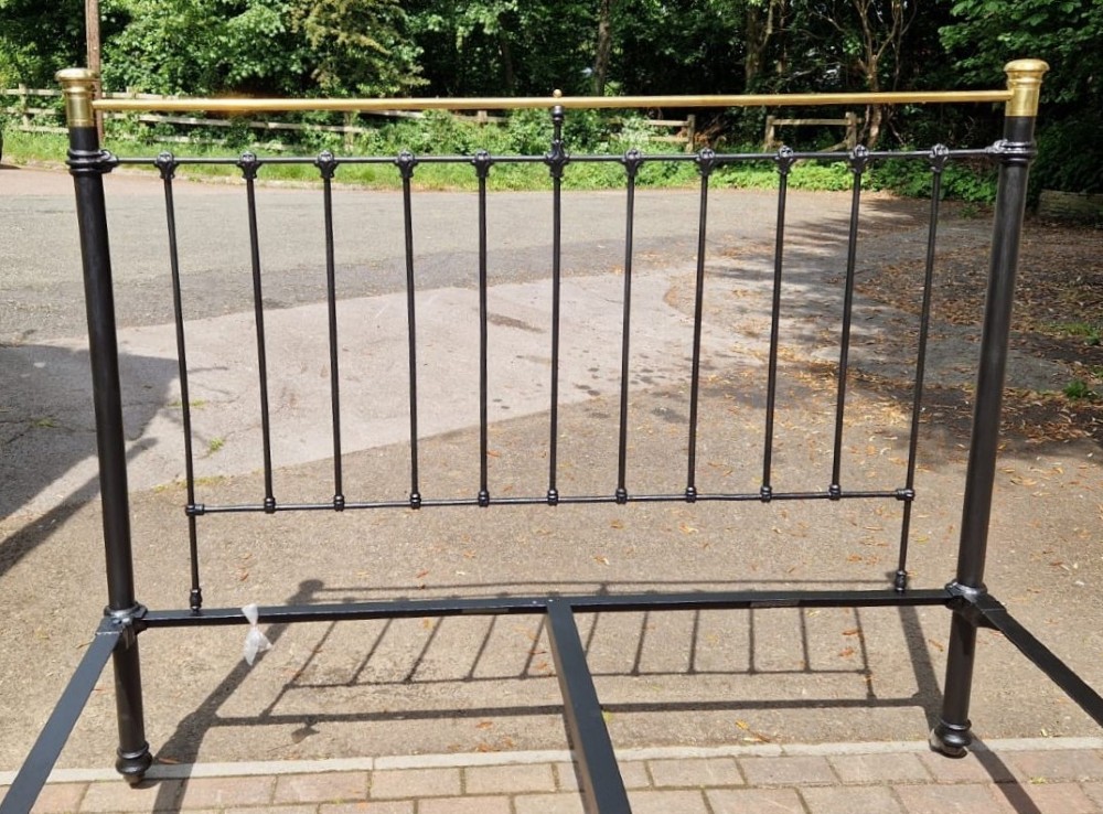A Victorian super king size bedstead featuring a black painted cast iron frame with vertical spindles and polished brass top rails and central motif. View II