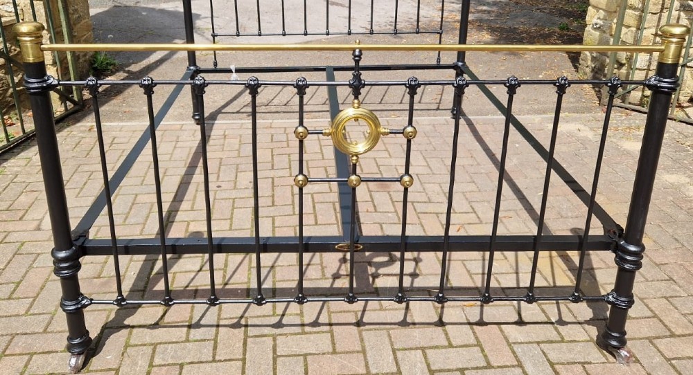 A Victorian super king size bedstead featuring a black painted cast iron frame with vertical spindles and polished brass top rails and central motif. View III
