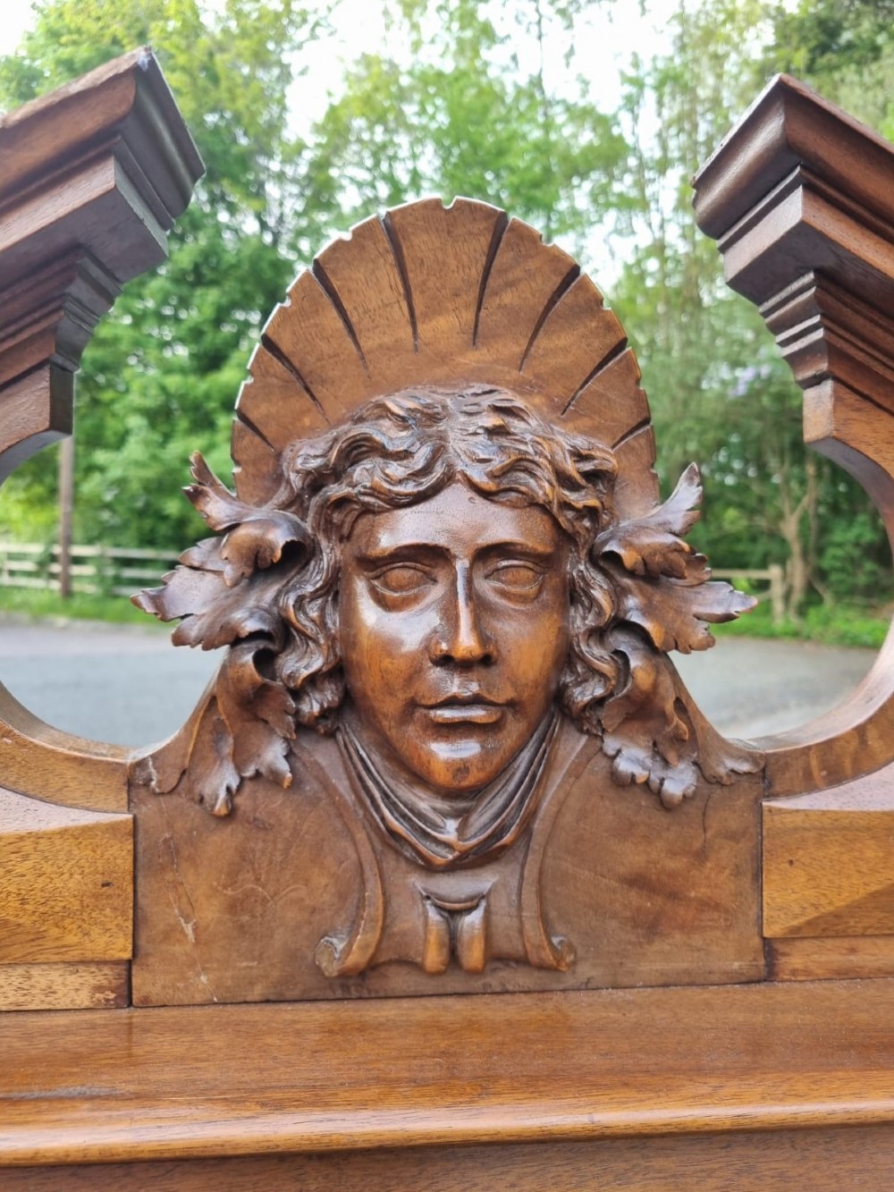 A 19th-century French carved walnut king size bedstead featuring a high panelled headboard topped with a carved face pediment and geometric starburst panels on the footboard. View IV