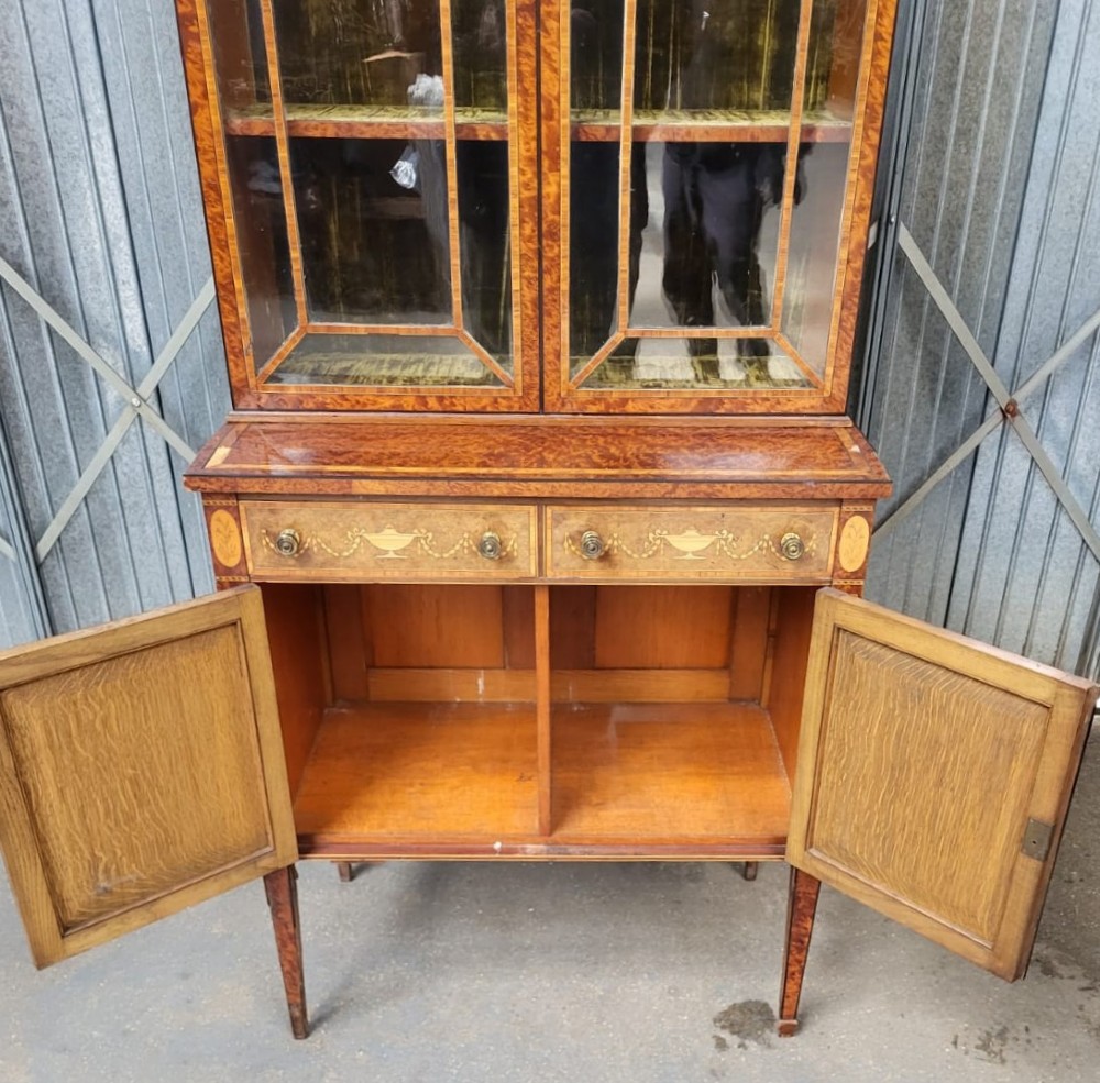 A Victorian birds eye maple bookcase featuring two glazed upper doors, inlaid drawers, marquetry lower cupboards, and tapered square legs. View II