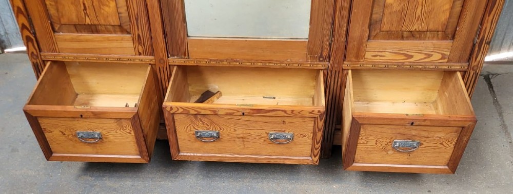 A large Victorian Arts and Crafts pitch pine wardrobe featuring three doors, an arched central mirror, geometric wood inlay, and three drawers at the base. View IX