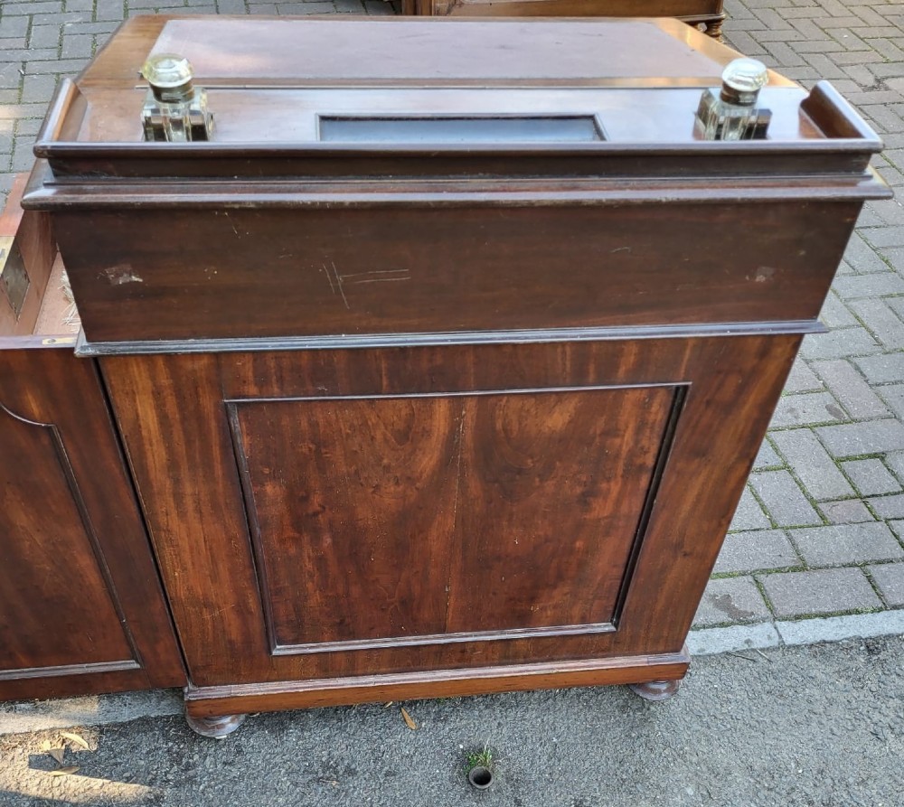 A Victorian mahogany Davenport desk featuring an inclined leather-inset writing surface, carved curved front supports, and a top gallery with glass inkwells. View IV