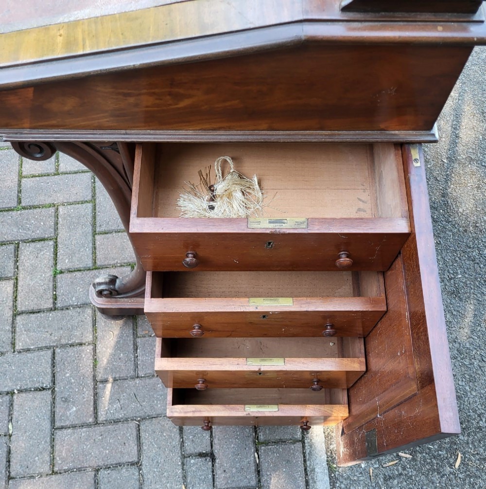 A Victorian mahogany Davenport desk featuring an inclined leather-inset writing surface, carved curved front supports, and a top gallery with glass inkwells. View V