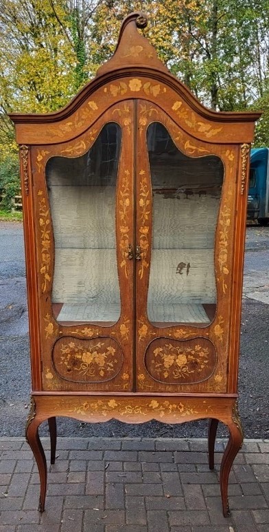 An Edwardian mahogany display cabinet featuring extensive floral marquetry inlay, curved glass doors, a shaped pediment, and cabriole legs.
