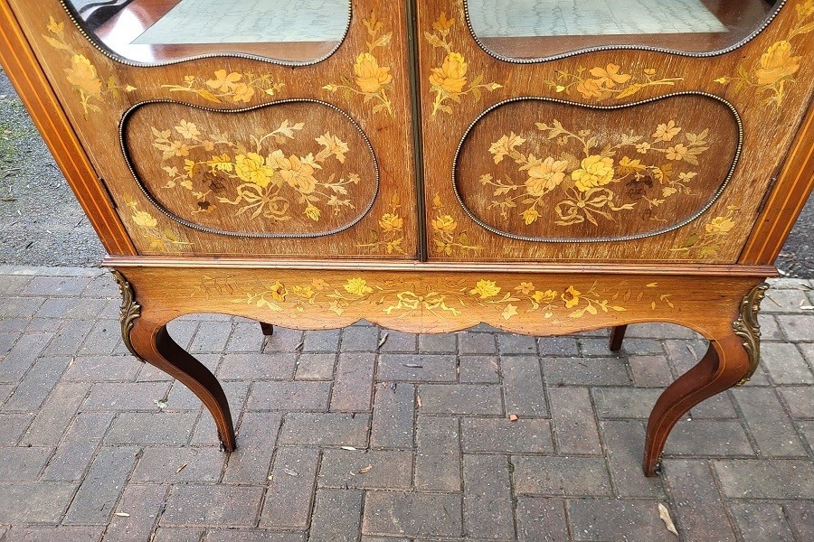 An Edwardian mahogany display cabinet featuring extensive floral marquetry inlay, curved glass doors, a shaped pediment, and cabriole legs. View II