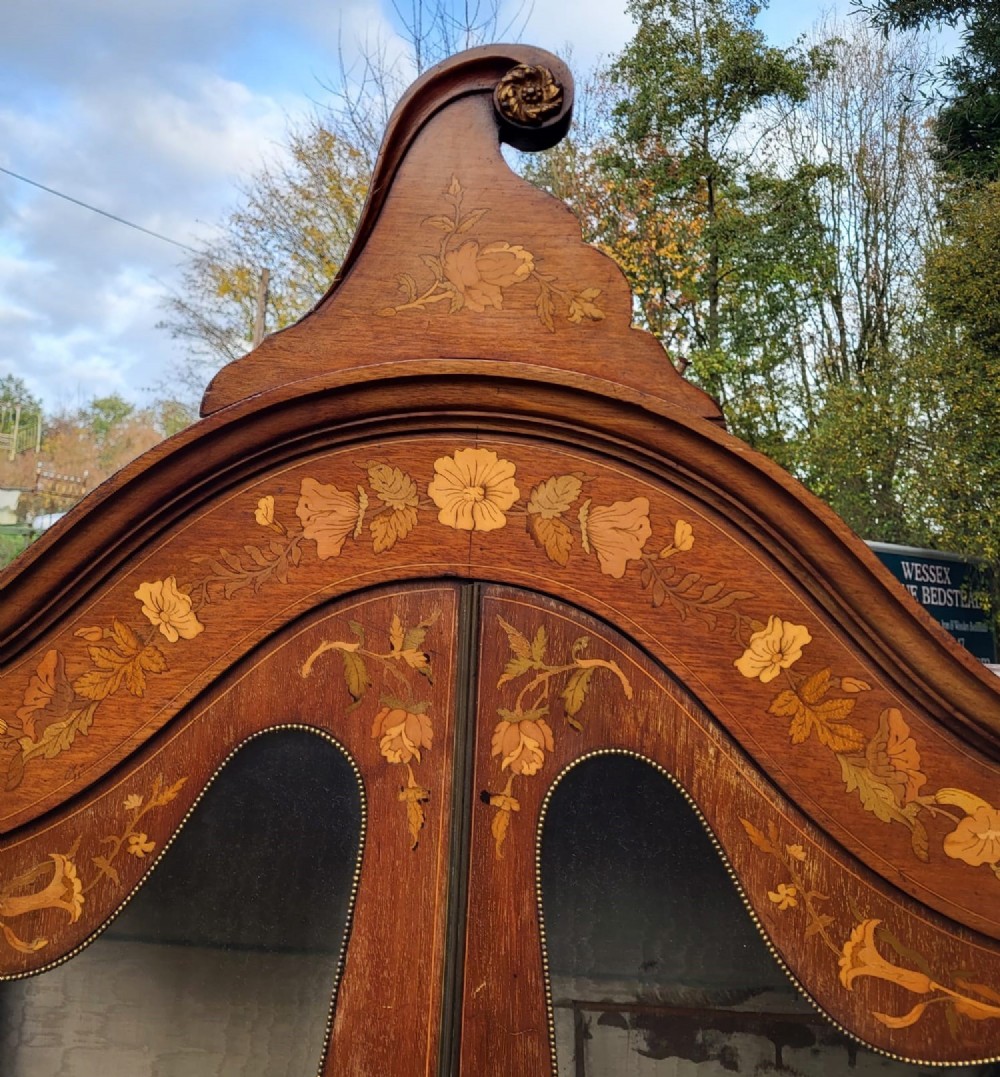 An Edwardian mahogany display cabinet featuring extensive floral marquetry inlay, curved glass doors, a shaped pediment, and cabriole legs. View V
