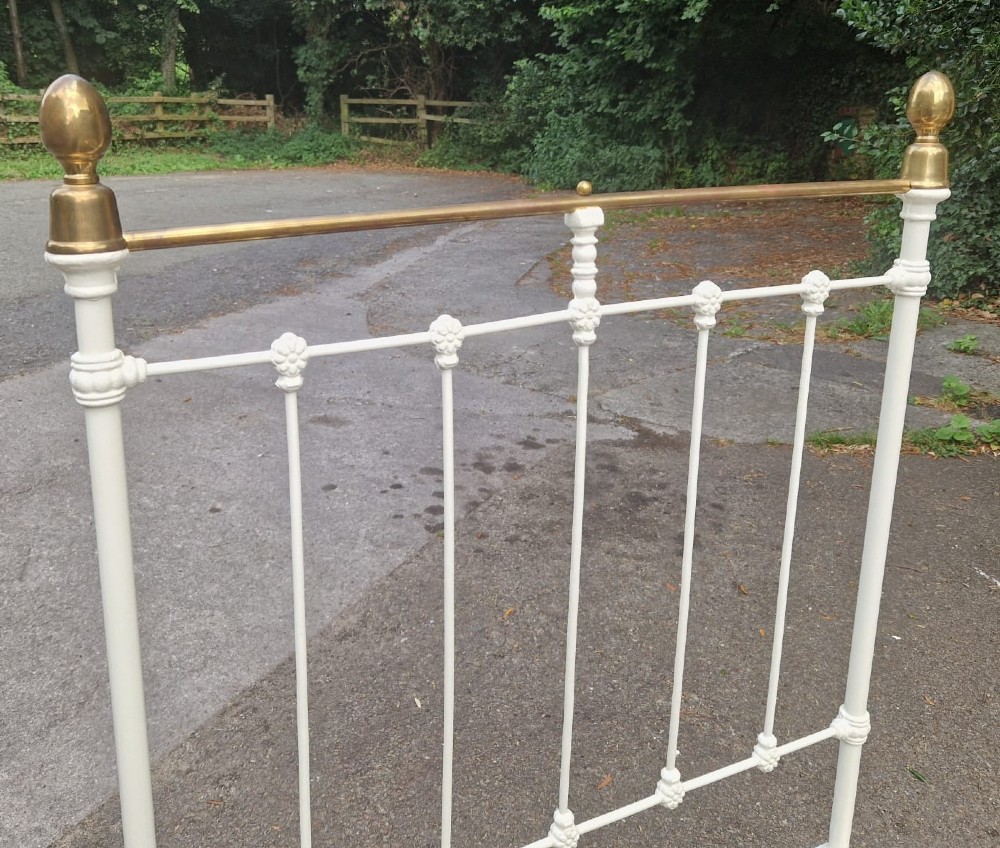 A single Victorian bedstead made of off-white painted cast iron with vertical spindles, a tubular brass top rail, and brass finials. View II