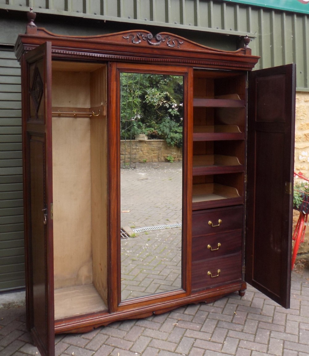 A late Victorian mahogany triple door wardrobe featuring a central full-length mirror, carved diamond relief panels, and a carved crest pediment. View II