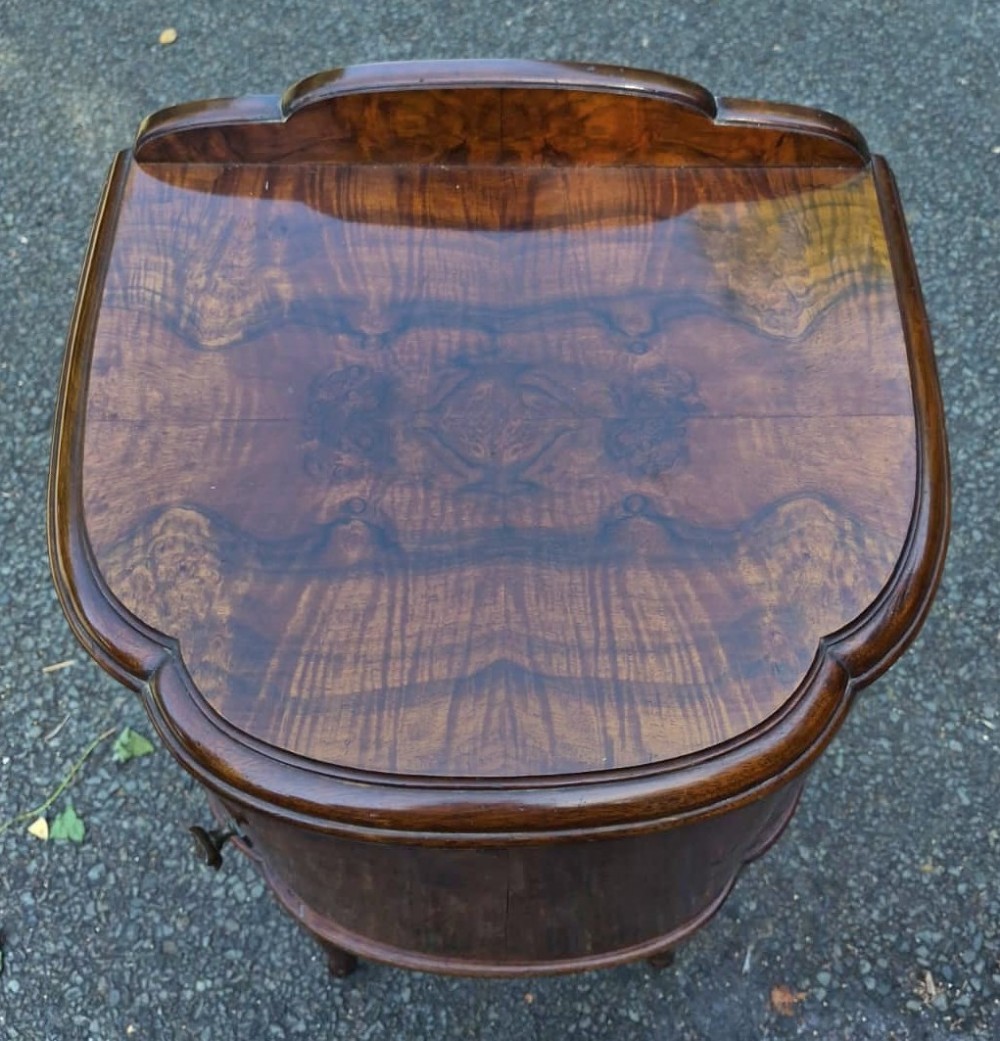 A seven-piece Art Deco bedroom suite crafted in burr walnut with arched tops, featuring a large wardrobe, triple-mirror dressing table, tallboy chest, bedside cupboard, stool, and two chairs. View VIII
