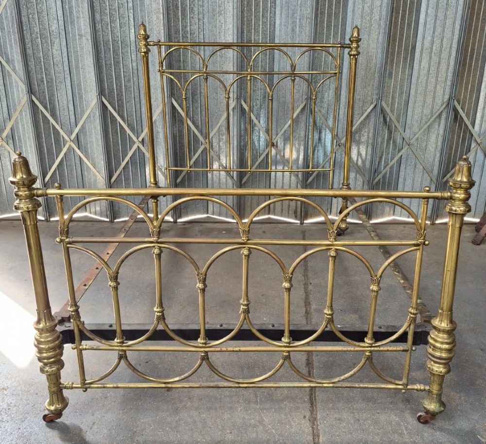 Victorian brass king-size bedstead featuring Gothic tracery arch designs on the headboard and footboard with decorative corner finials.