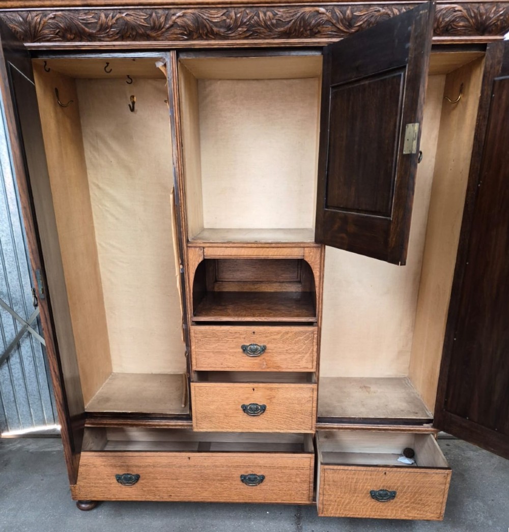 A six-piece golden oak Arts and Crafts bedroom suite including a central compactum wardrobe with mirrors, a dressing chest, a desk, a pot cupboard, and two rush-seat chairs. View III