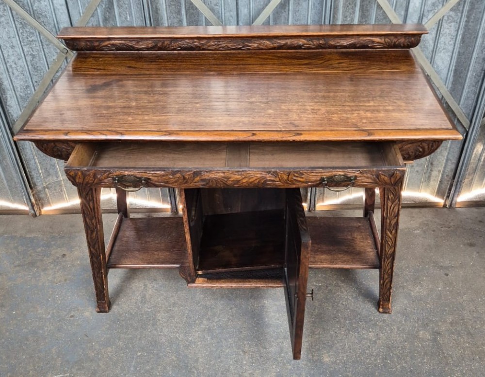 A six-piece golden oak Arts and Crafts bedroom suite including a central compactum wardrobe with mirrors, a dressing chest, a desk, a pot cupboard, and two rush-seat chairs. View VIII
