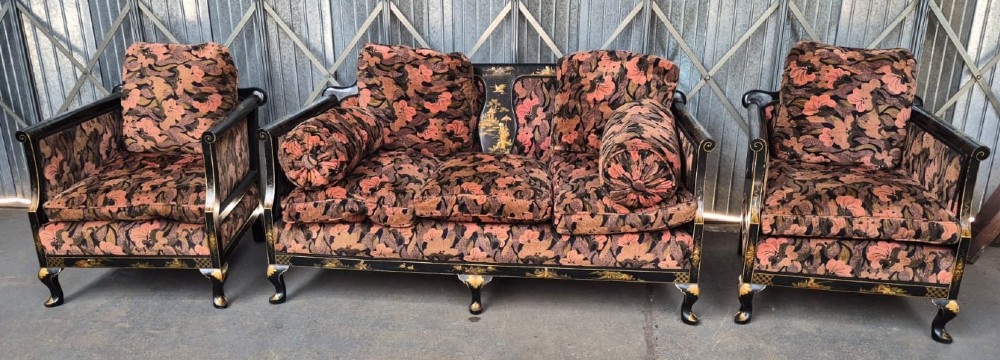 A three-piece Edwardian seating suite comprising a central two-seater settee and two matching armchairs with black lacquered frames adorned with gilded Chinoiserie patterns and pink floral pattern fabric upholstery.