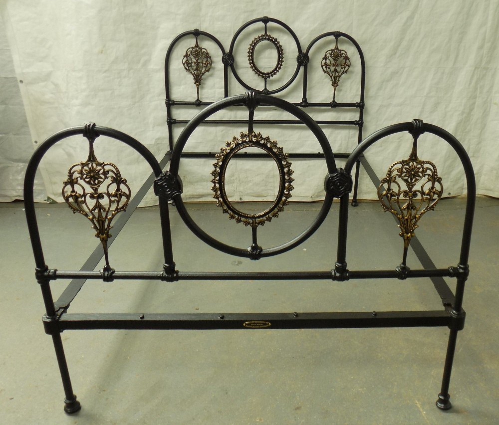 A Victorian double iron bedstead featuring a black tubular frame with arched top rails and central circular medallions with gold filigree detail.