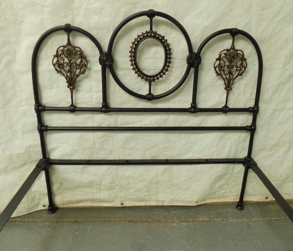 A Victorian double iron bedstead featuring a black tubular frame with arched top rails and central circular medallions with gold filigree detail. View II
