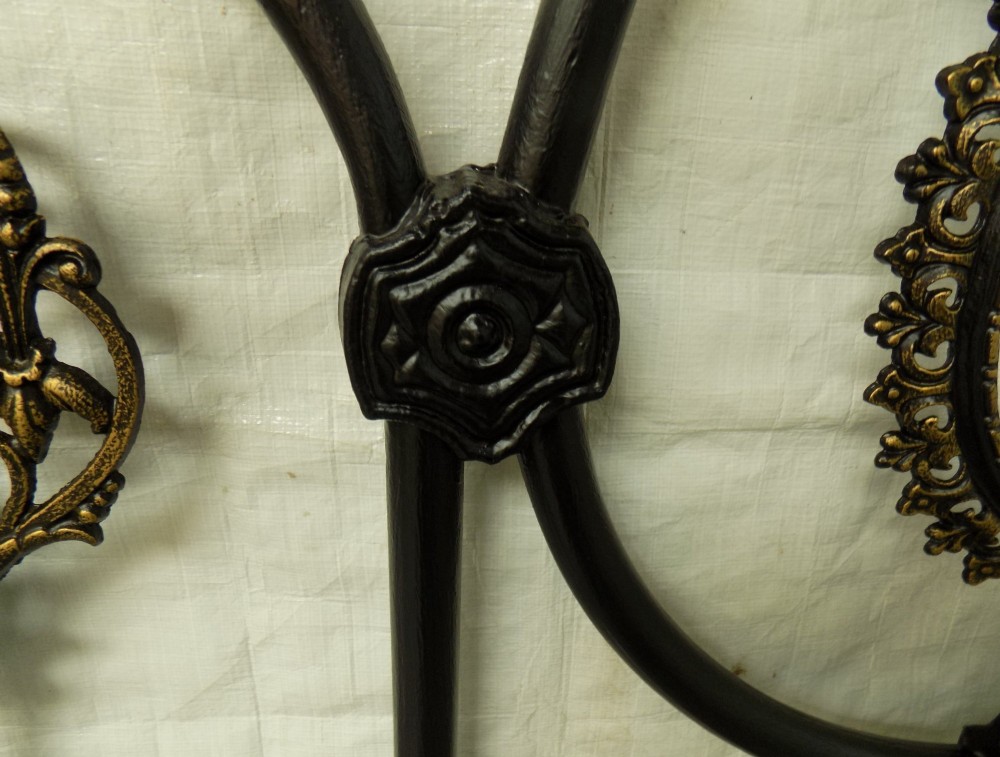 A Victorian double iron bedstead featuring a black tubular frame with arched top rails and central circular medallions with gold filigree detail. View VIII