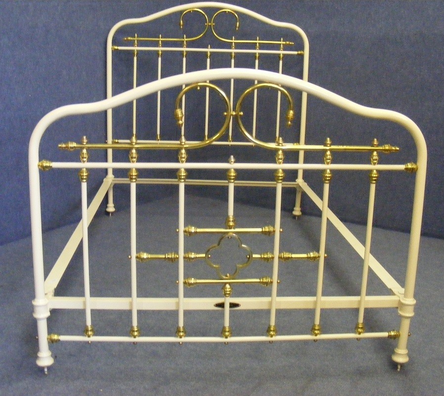A Victorian small double bedstead featuring a cream-painted iron frame with ornate polished brass rails, finials, and scrollwork.