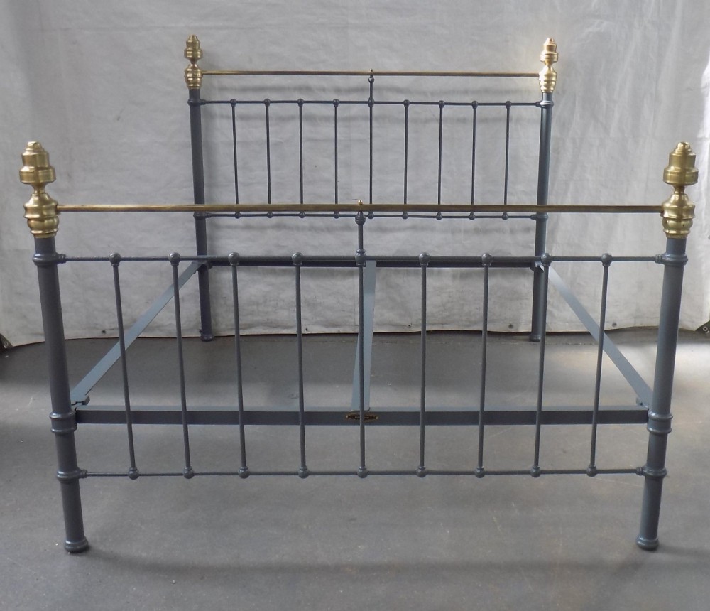 A Victorian grey painted iron bedstead featuring vertical spindles, horizontal brass top rails, and decorative brass corner finials.