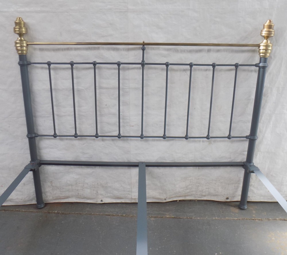 A Victorian grey painted iron bedstead featuring vertical spindles, horizontal brass top rails, and decorative brass corner finials. View II