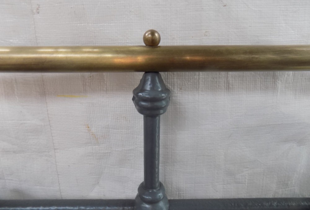 A Victorian grey painted iron bedstead featuring vertical spindles, horizontal brass top rails, and decorative brass corner finials. View V