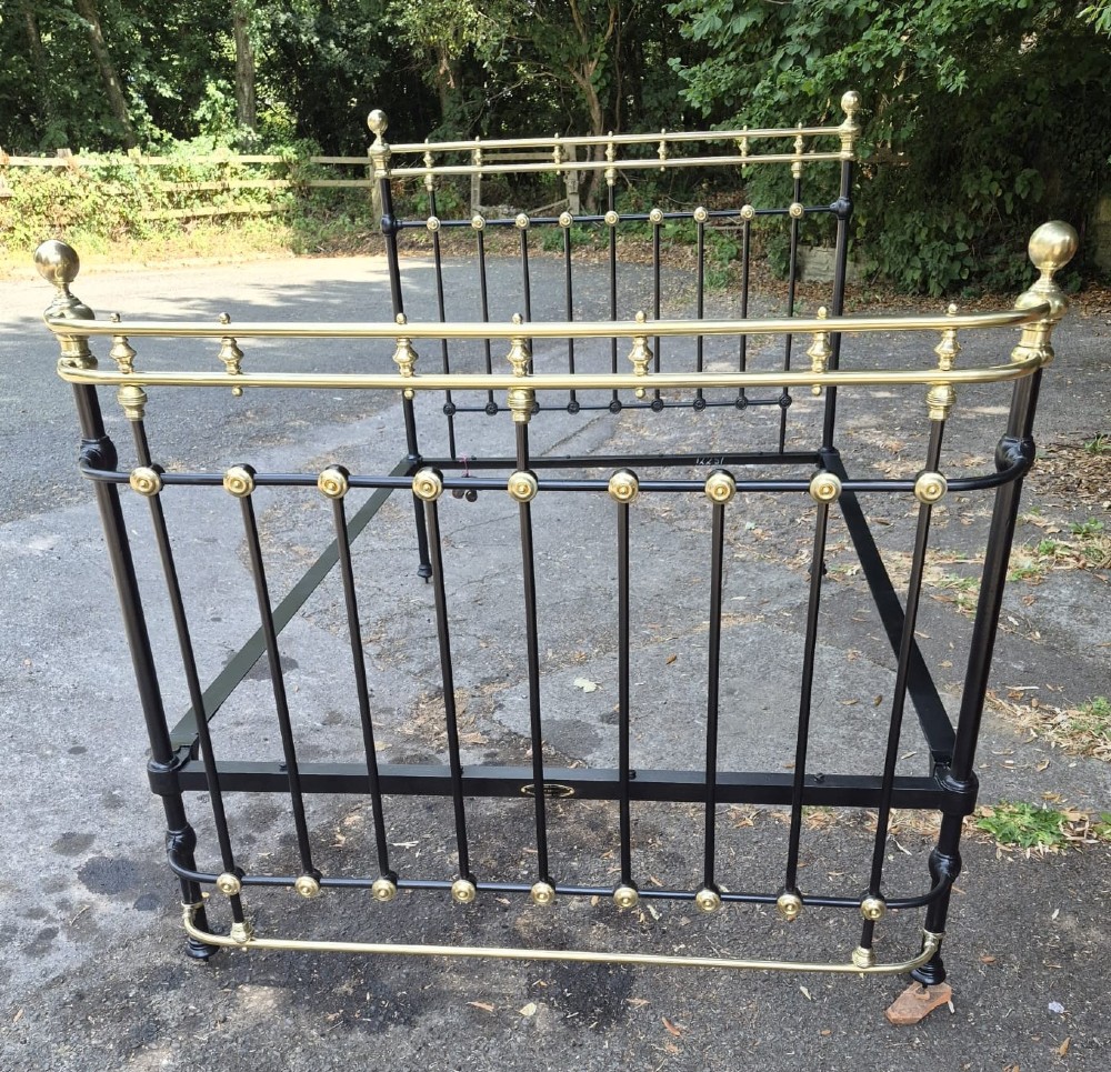 A Victorian double-size black iron bedstead featuring polished brass top rails, brass vertical mounts, and ball finials.