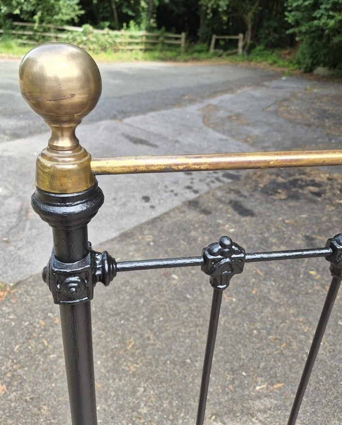 A king size Victorian wrought iron bedstead featuring a black painted frame, vertical upright spindles with cast decorative collars, and a polished brass top bar with brass urn finials. View II