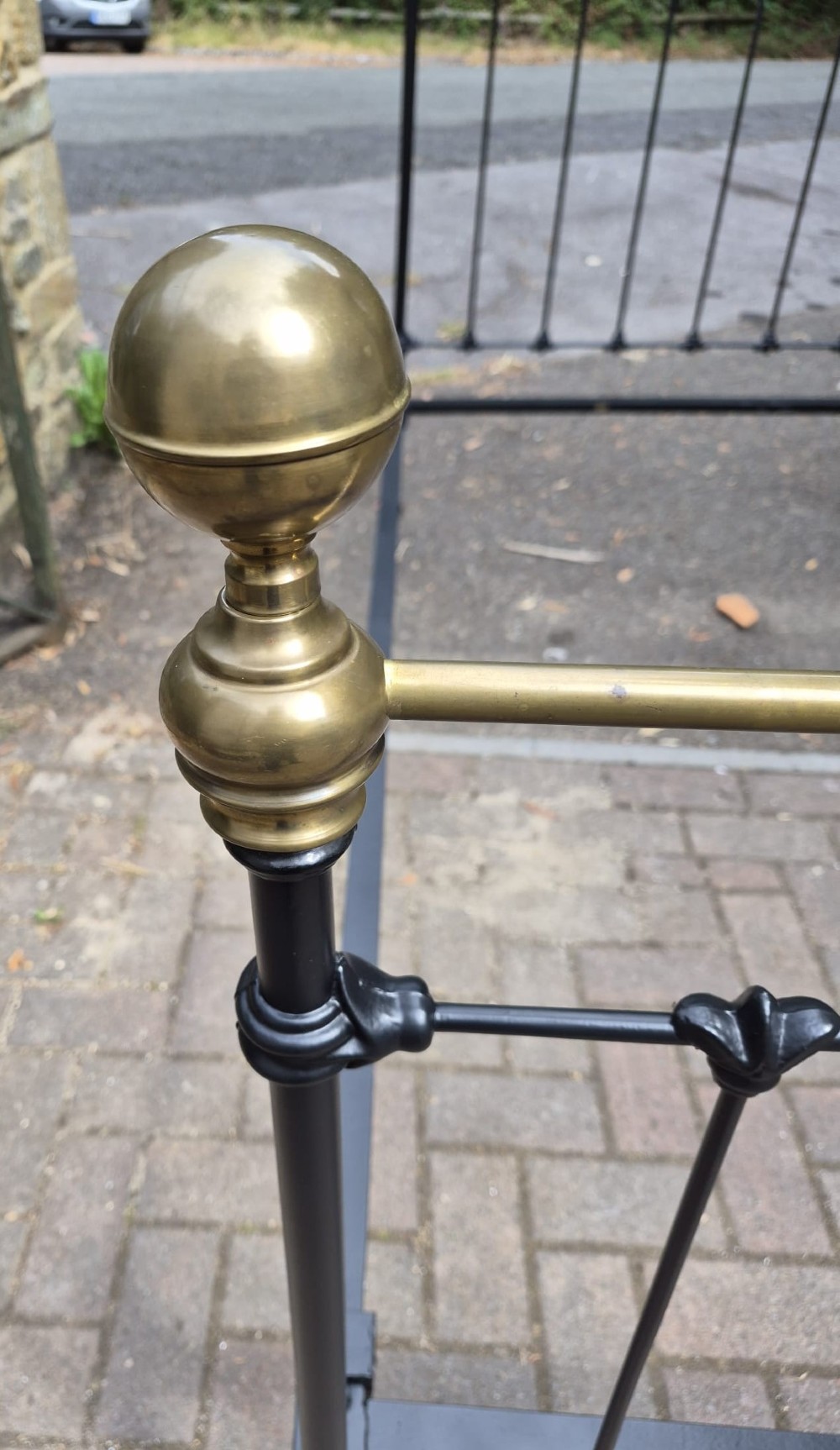 A matching pair of Victorian black iron single bedsteads featuring vertical spindles, cast floral embellishments, and polished brass top rails with spherical finials. View II