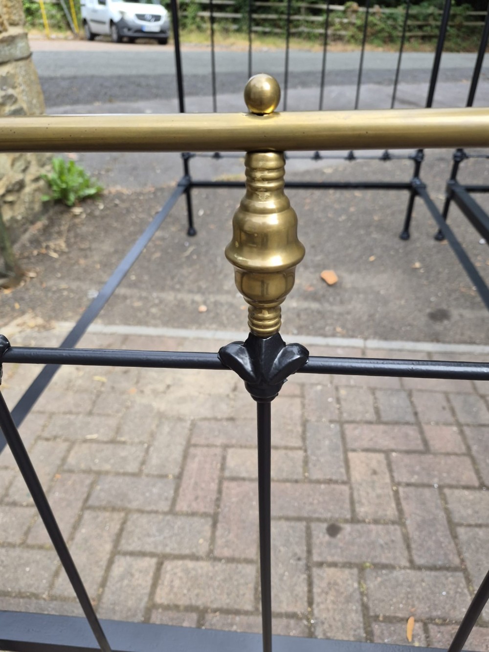 A matching pair of Victorian black iron single bedsteads featuring vertical spindles, cast floral embellishments, and polished brass top rails with spherical finials. View III