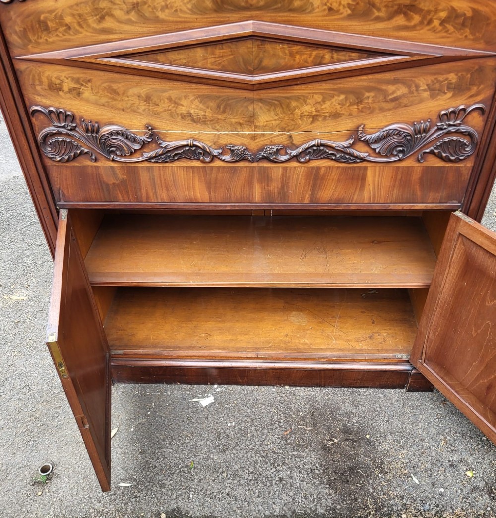 A 19th-century flame mahogany secretaire a abattant featuring carved scrollwork, diamond veneer patterns, lower cupboards with rosette medallions, and a brass gallery top. View III