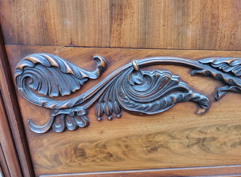 A 19th-century flame mahogany secretaire a abattant featuring carved scrollwork, diamond veneer patterns, lower cupboards with rosette medallions, and a brass gallery top. View V