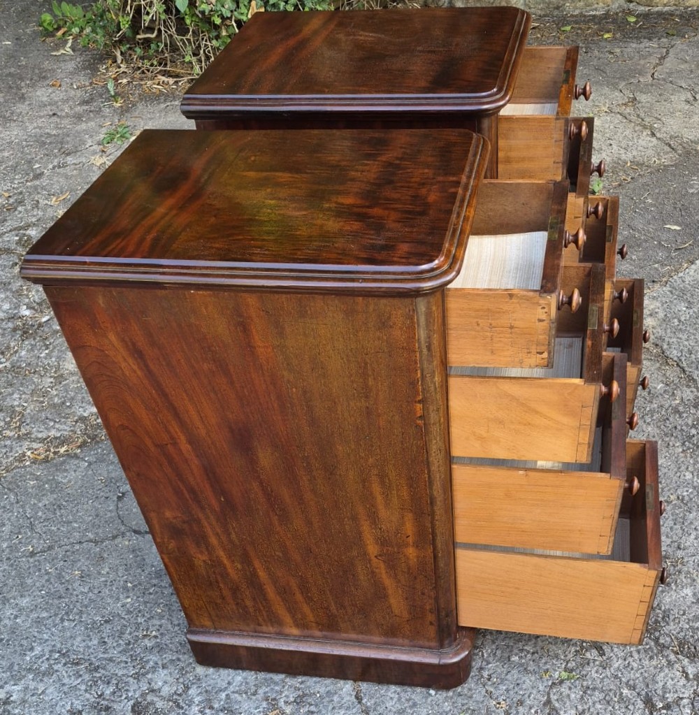 A matching pair of narrow Victorian mahogany bedside chests featuring four drawers each with turned wooden knobs and brass escutcheons on a solid plinth base. View V