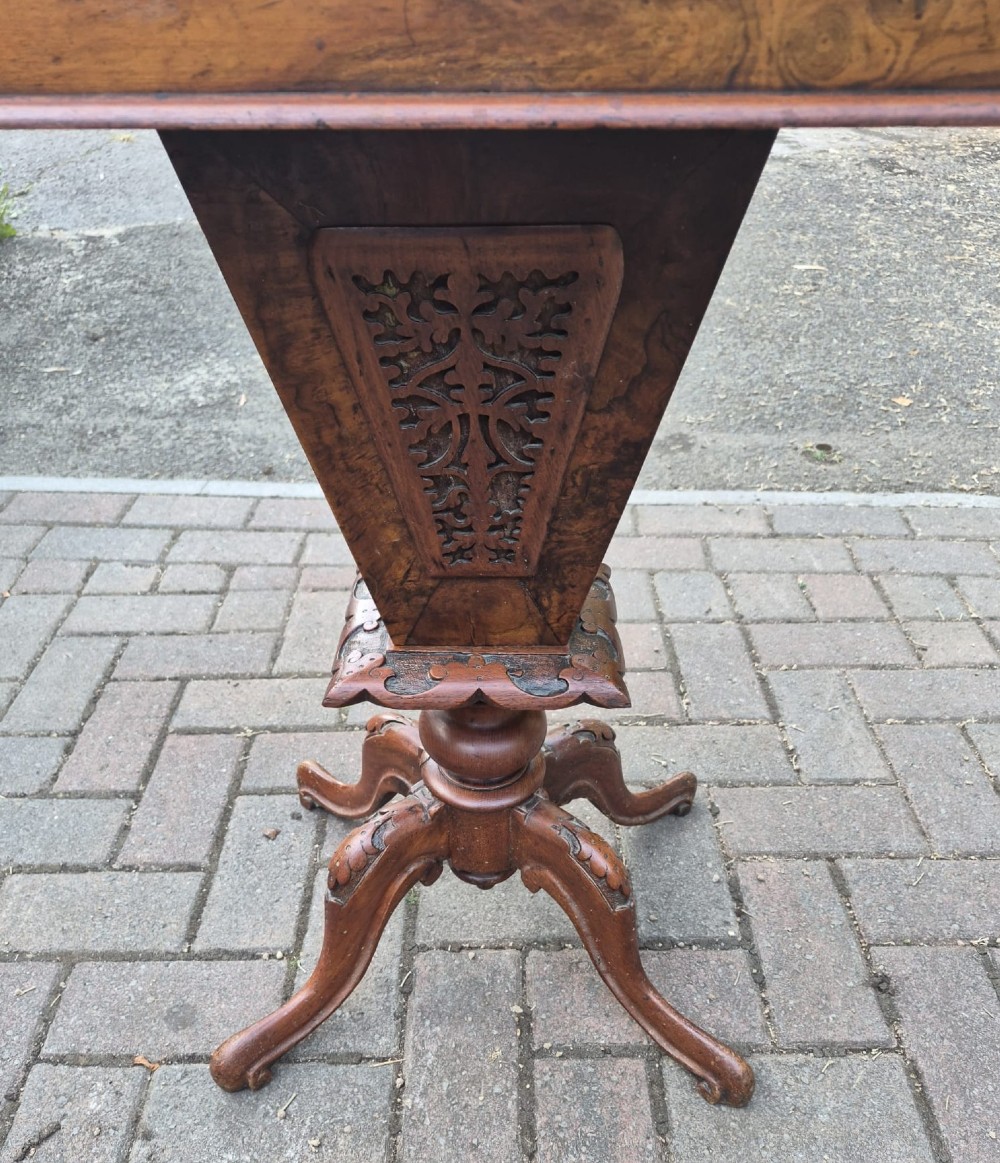A Victorian burr walnut sewing table featuring a rectangular hinged top, a tapering fretwork work well, and a carved pedestal base resting on four cabriole legs. View IV