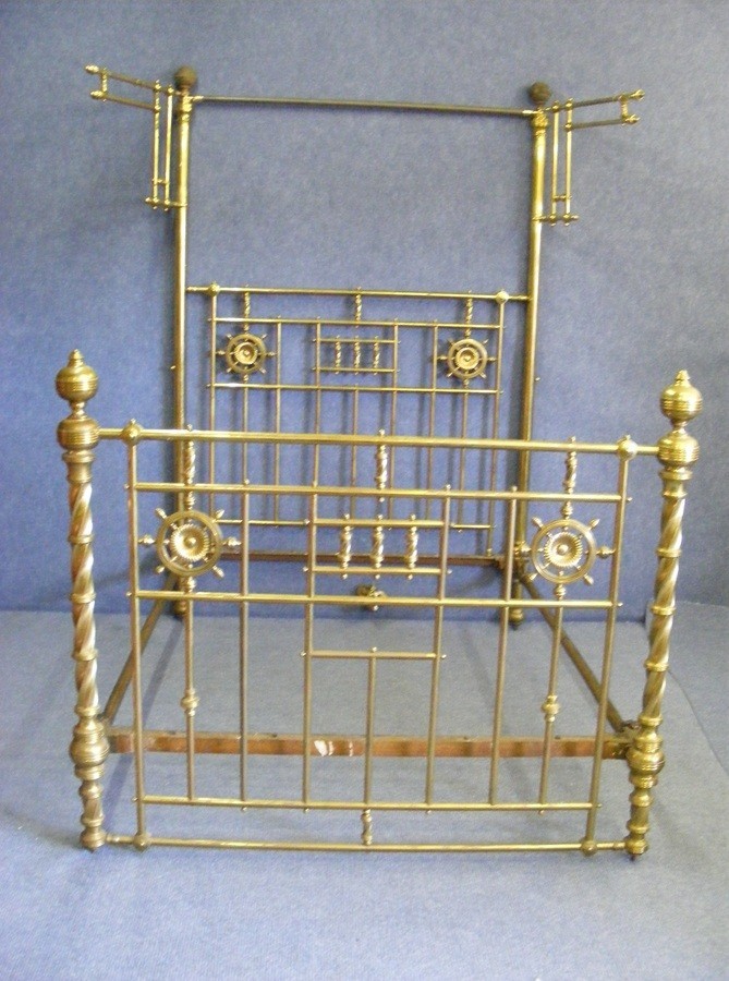 A Victorian king size brass half tester bedstead with barley twist posts, geometric vertical spindles, wheel motifs, and an upper canopy frame.