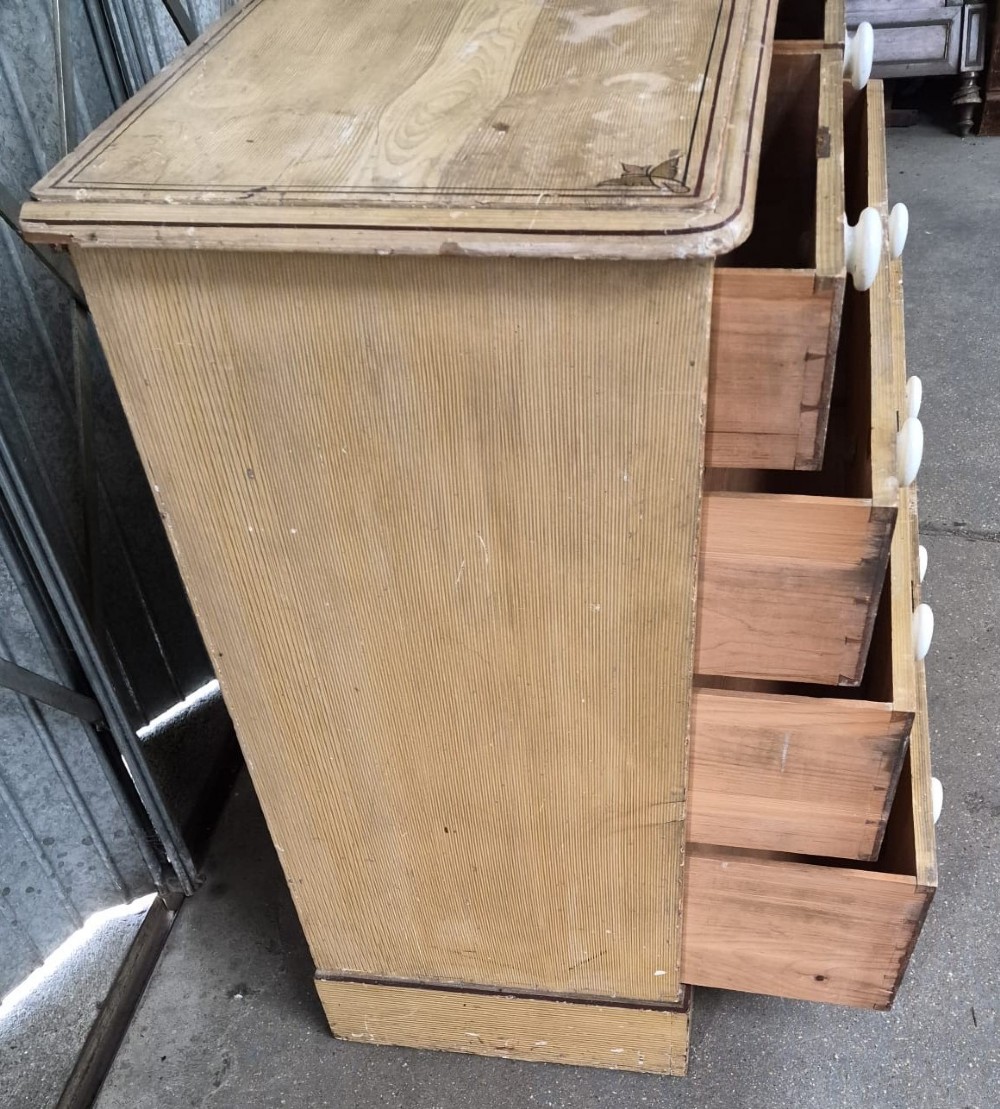 A Victorian pine chest of drawers featuring two short drawers over three long drawers with white ceramic knobs and printed corner line motifs. View III