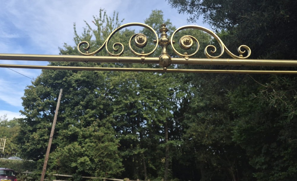 A Victorian brass half tester bedstead featuring an intricate scrolled headboard, turned corner posts, decorative finials, and an upper canopy frame. View V