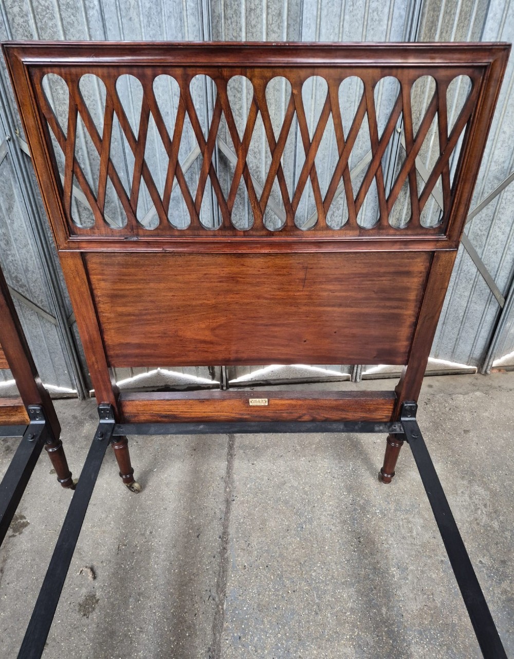 A pair of Edwardian mahogany single bed frames featuring pierced lattice upper panels, flame mahogany lower panels, turned legs, and brass castors. View II