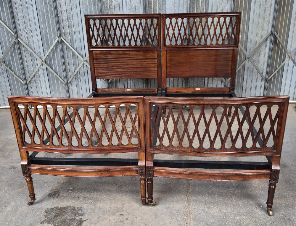A pair of Edwardian mahogany single bed frames featuring pierced lattice upper panels, flame mahogany lower panels, turned legs, and brass castors. View V