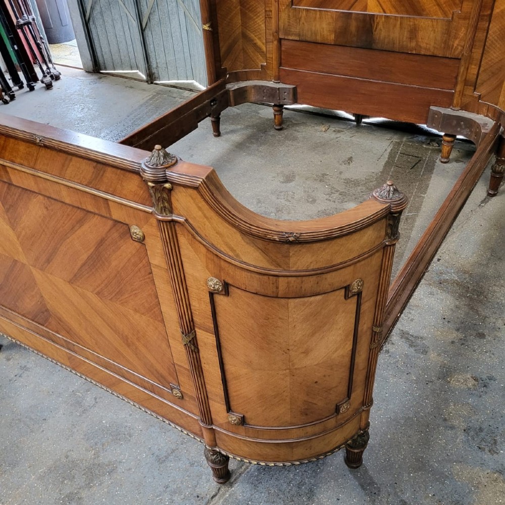 A 19th-century French king-size bedstead made from quarter-veneered walnut with carved cresting and gilt bronze mounts on the headboard and footboard. View VI