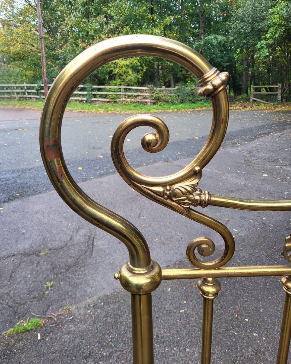 An antique Victorian brass king size bedstead featuring scrolled top rails, vertical spindles, floral cast cartouches, and metal castors. View III