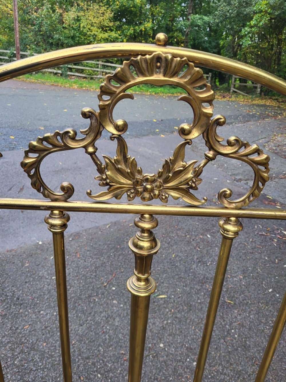 An antique Victorian brass king size bedstead featuring scrolled top rails, vertical spindles, floral cast cartouches, and metal castors. View IV