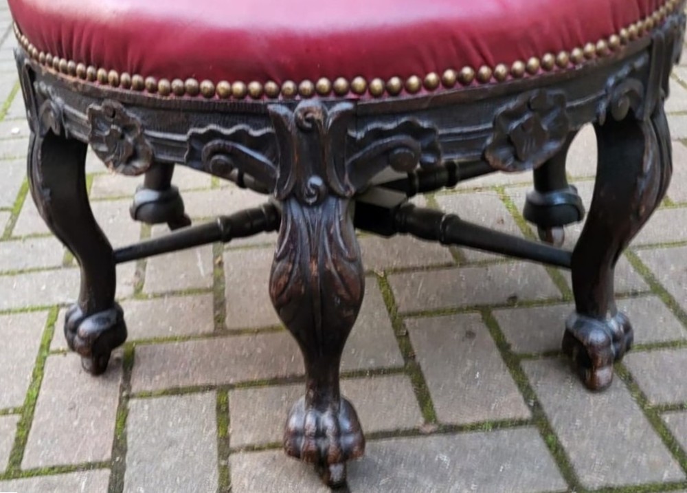 A Victorian carved dark oak Burgomaster chair with a curved back rail, carved oval panels, and a red leather circular seat with brass stud details. View IV