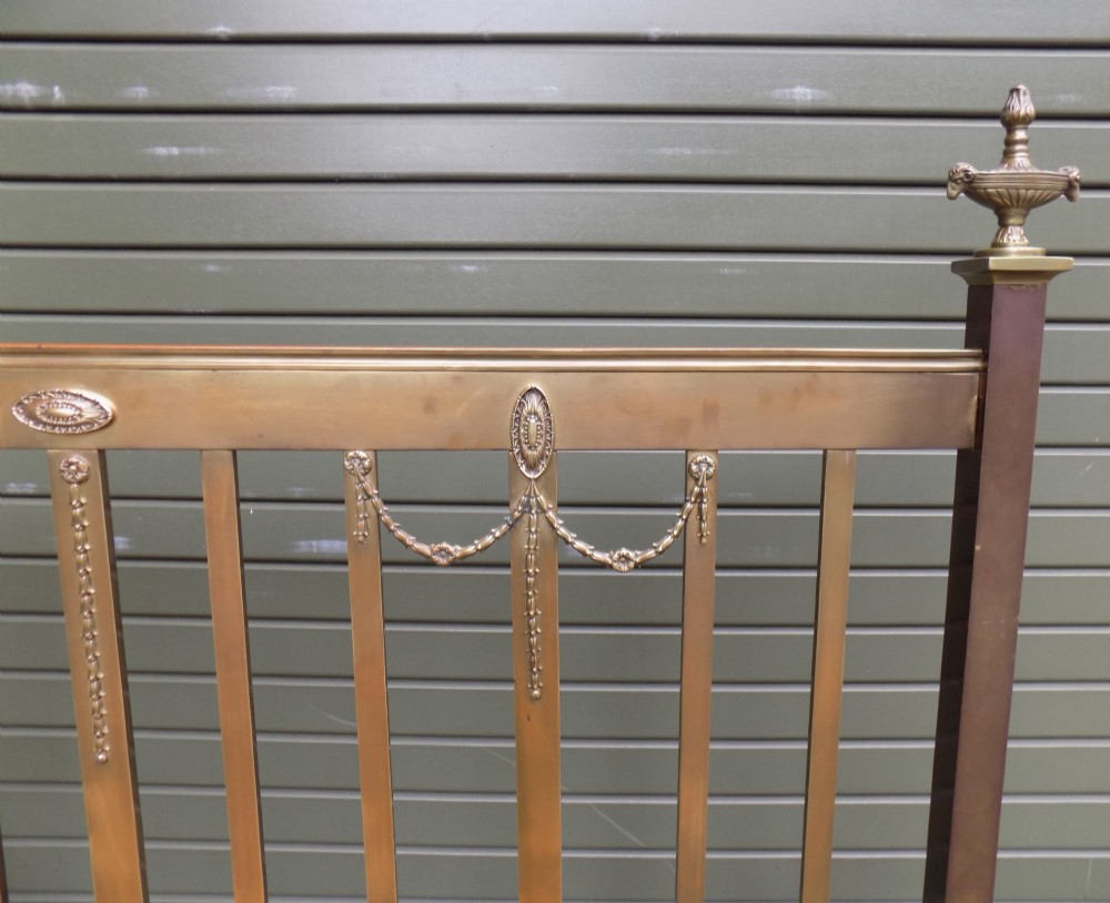 An antique Victorian brass bedstead with decorative urn finials, vertical spindles, ribbon swags, and castors. View IV