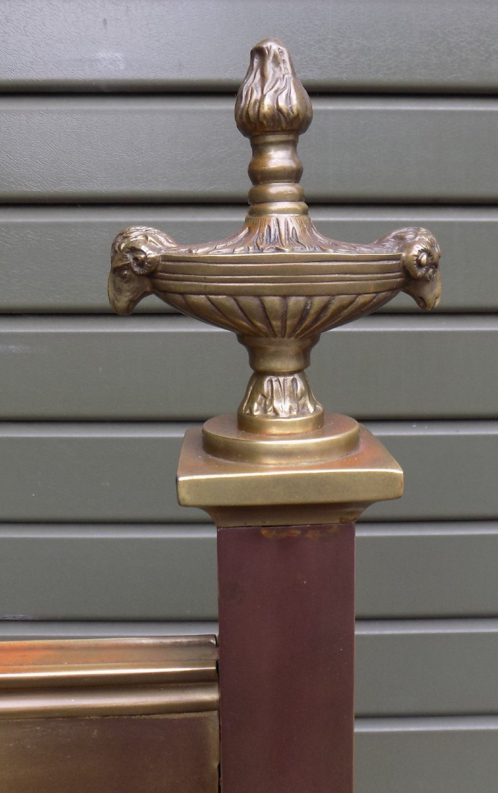 An antique Victorian brass bedstead with decorative urn finials, vertical spindles, ribbon swags, and castors. View V